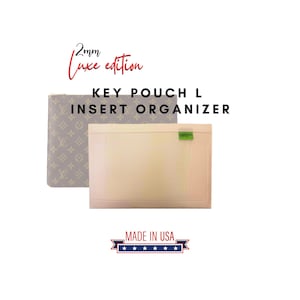 Può includere: Un organizer a inserto Key Pouch L edizione 2mm Luxe prodotto negli USA. Il prodotto presenta una pochette rettangolare beige chiaro con una piccola etichetta verde, posizionata davanti a una pochette grigia con un motivo monogramma chiaro.