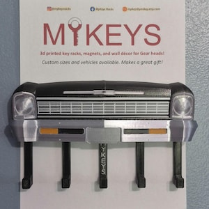 May include: A black and silver key rack shaped like a car front, with four key hooks. The rack has a black top, silver bumper, and the text "MYKEYS" and "YKEYS". The image also includes the text "3d printed key racks, magnets, and wall décor for Gear heads!"