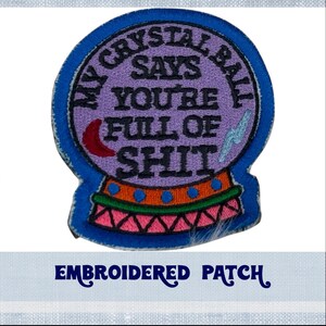 May include: Embroidered patch of a purple crystal ball with the text "My Crystal Ball Says You're Full Of Shit". The crystal ball is surrounded by a blue, green, orange, and pink border.