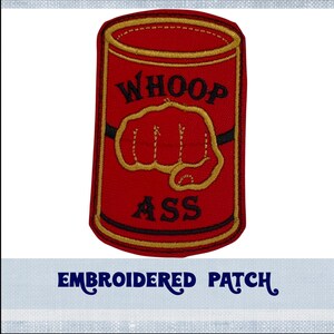 May include: Red embroidered patch shaped like a can with the words "WHOOP ASS" and a cartoon fist on it. The patch has a gold outline and black lettering. The words "EMBROIDERED PATCH" are printed below the patch.