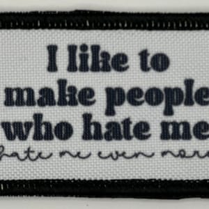 May include: A rectangular patch with a white background and black text that reads "I like to make people who hate me, hate me even more." The patch has a black border.