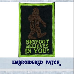 May include: Embroidered patch with a green border, featuring a brown Bigfoot figure with green eyes and the text "BIGFOOT BELIEVES IN YOU!"
