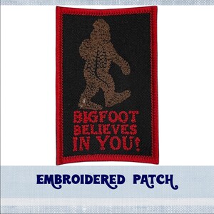 May include: Embroidered patch with a red border. The patch features a brown Bigfoot silhouette walking with the text "BIGFOOT BELIEVES IN YOU!" in red.
