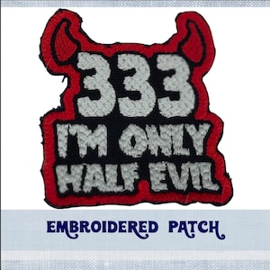Könnte beinhalten: Gestickter Aufnäher mit roten Teufelshörnern, schwarzem Hintergrund und weißem Text, der "333 I'm only half evil" lautet.