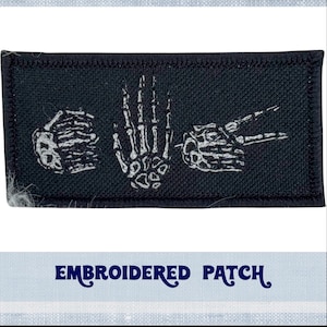 Könnte beinhalten: Schwarzer gestickter Aufnäher mit drei weißen Skeletthänden in verschiedenen Positionen. Der Aufnäher trägt unten den Schriftzug "EMBROIDERED PATCH".
