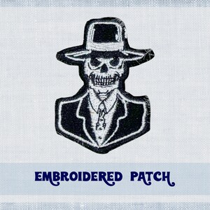 May include: Embroidered patch of a skeleton wearing a suit and a fedora hat. The patch is black and white.