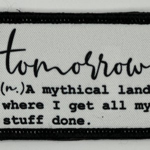 Könnte beinhalten: Ein weißer Stoff-Patch mit schwarzen Nähten und schwarzem Text, der "tomorrow (n.) A mythical land where I get all my stuff done." lautet.
