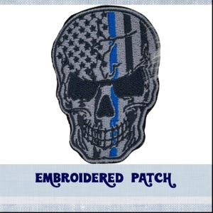 May include: Embroidered patch featuring a skull design with an American flag motif. The skull has a blue line running down the center. The patch is gray, black, and blue.