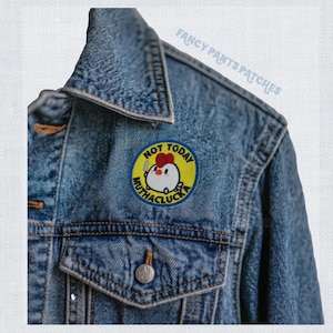 May include: A blue denim jacket with a yellow and red embroidered patch that says "Not Today Mutha Clucka" and features a cartoon chicken holding a knife.