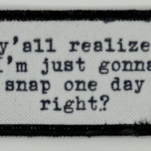 May include: A rectangular patch with a black border and white background. The text "y'all realize I'm just gonna snap one day right?" is printed in black, typewriter-style font. The patch is likely made of fabric.