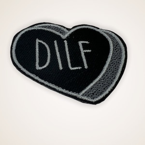 May include: Black heart-shaped patch with gray stitching and the word "DILF" embroidered in white.