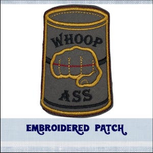 May include: Embroidered patch featuring a grey can with a yellow rim. The can displays the words "WHOOP ASS" and a gold fist with red stitching.