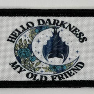 May include: A rectangular fabric patch with a black border featuring a white background. The text HELLO DARKNESS MY OLD FRIEND surrounds a central graphic of a dark blue bat hanging from a crescent moon, accented by blue and green floral details.
