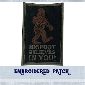 May include: Embroidered patch featuring a brown Bigfoot figure walking on a black background. The text "BIGFOOT BELIEVES IN YOU!" is below the figure. The patch has a green border.
