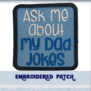 Puede incluir: Parche bordado azul y blanco con el texto "Ask me about my dad jokes" sobre un fondo azul. El parche tiene un borde negro y el texto "Embroidered Patch" está impreso debajo del parche.