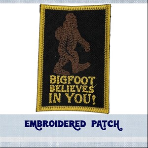 May include: Embroidered patch with a brown Bigfoot silhouette and the text "BIGFOOT BELIEVES IN YOU!" in yellow thread on a black background. The patch has a gold border.