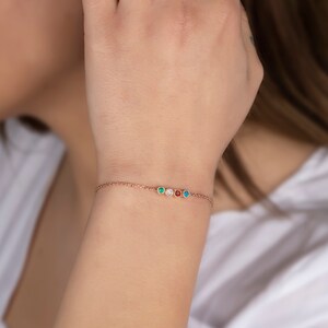 Op de afbeelding: Een delicate gouden kettingarmband met vijf kleine ronde edelstenen. De edelstenen zijn groen, wit, blauw, oranje en rood.