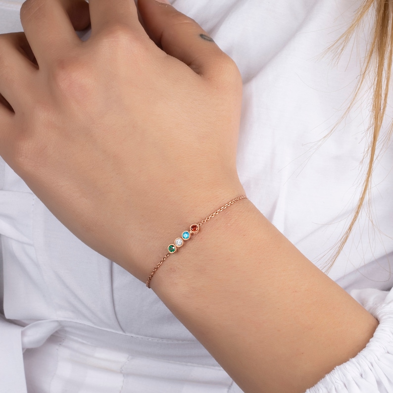 Op de afbeelding: Een delicate gouden kettingarmband met vijf kleine ronde edelstenen in verschillende kleuren: groen, blauw, wit, turquoise en rood.