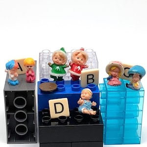 May include: A set of colorful plastic figurines of children, some wearing hats, arranged on a multi-colored Lego base with letter blocks that spell out "A, B, D".