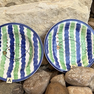 May include: Two blue and green striped ceramic plates with a white background and a black fish design. The plates are labeled A and B.