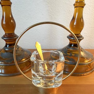 May include: A gold metal ring stand with a clear glass salt cellar and a small gold spoon. The stand is in front of two amber glass candle holders.