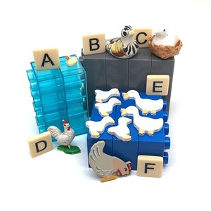 May include: A blue and gray toy block set with letters A through F, a white rooster, a white duck, a yellow duck, and a white duck in a nest. The set includes a variety of farm animals and letters.
