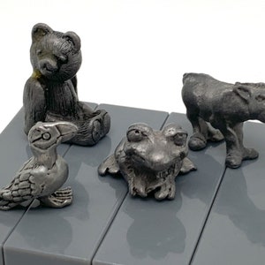 May include: A set of four pewter figurines, including a bear, a frog, a bird, and a donkey. The figurines are all in a sitting or standing position and are made of a silver-colored metal.