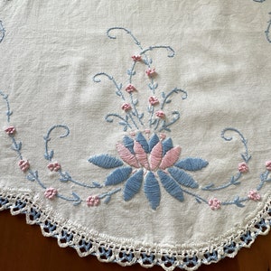 May include: A white crocheted doily with a blue and pink embroidered floral design.