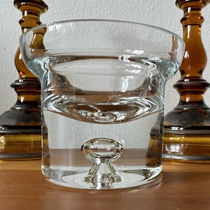 May include: A clear glass bowl with a unique bubble design in the center. The bowl is sitting on a wooden surface.