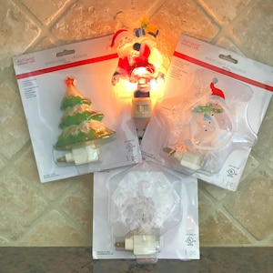 May include: A white ceramic mug with a black handle and the text "But First, Coffee" in a bold, black font. The mug is set against a blurred background, suggesting a cozy setting.