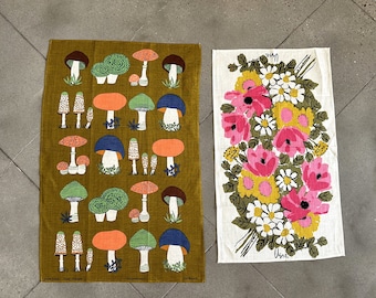 May include: Two kitchen towels, one with a mushroom pattern on a green background and the other with a floral pattern on a white background. The mushroom towel has the text "Frida Kahlo" and "Old Branch" printed on it. The floral towel has the text "Usma" printed on it.