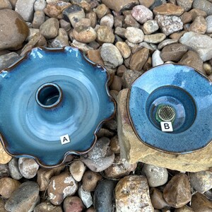 May include: Two blue ceramic dishes with a raised center. The dish on the left has a scalloped edge and the dish on the right is round. Both dishes have a glazed finish.