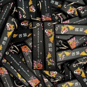May include: Black keychains with a Japanese koi fish design and the words "PARKED PRETTY" and Japanese characters. The keychains feature a metal ring and a colorful illustration of a koi fish and cherry blossoms.
