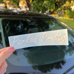 May include: A white sticker with the text "Parked Pretty" in pink script font. The sticker is on a blue background and has a slight sheen.