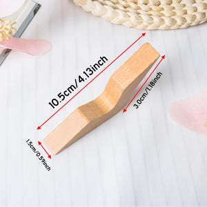 May include: A light-colored wooden object with a curved design, measuring 4.13 inches long, 1.18 inches wide, and 0.59 inches thick. The object is displayed on a white surface with pink floral accents and a woven coaster.