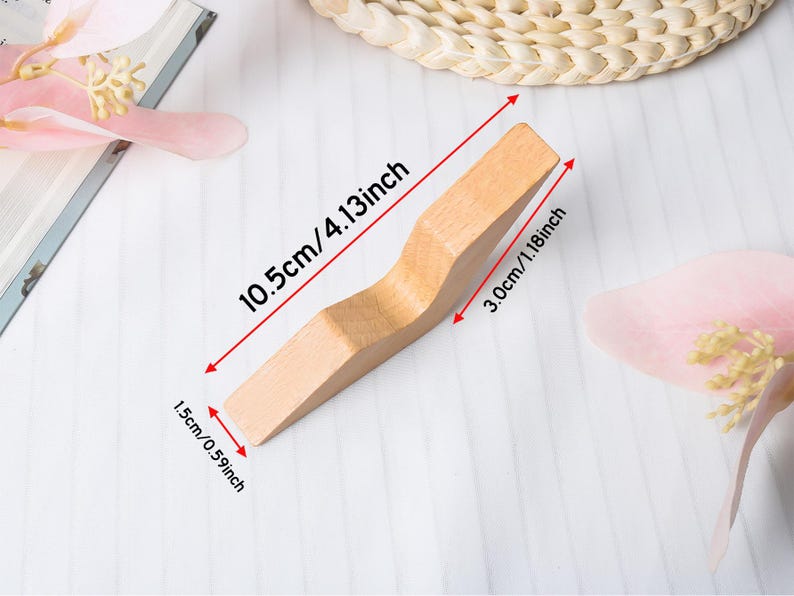 May include: A light-colored wooden object with a curved design, measuring 4.13 inches long, 1.18 inches wide, and 0.59 inches thick. The object is displayed on a white surface with pink floral accents and a woven coaster.
