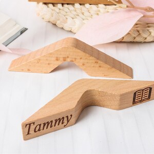 May include: Two wooden bookends in a light brown color. One bookend has the name "Tammy" engraved on it, and the other has a small book icon. The bookends are angled and have a unique shape.
