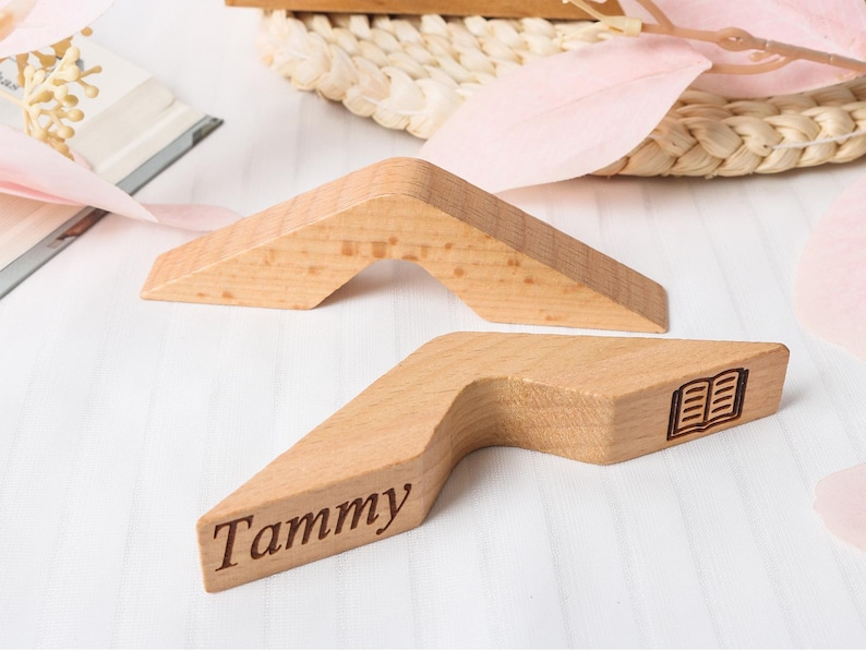 May include: Two wooden bookends in a light brown color. One bookend has the name "Tammy" engraved on it, and the other has a small book icon. The bookends are angled and have a unique shape.