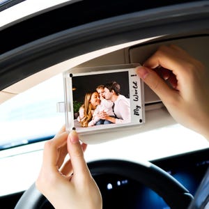 Op de afbeelding: Transparante acryl fotolijst met een familiefoto. De lijst wordt door de handen van een persoon omhoog gehouden. De foto toont een gezin van drie personen. De tekst "My World!" staat op de lijst.