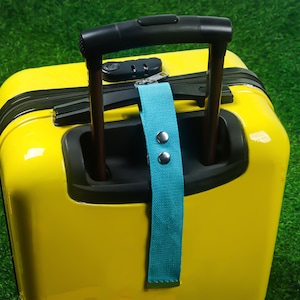 May include: A bright yellow suitcase with a black handle and a teal luggage tag. The suitcase has a combination lock and a zipper closure. The teal tag is secured with two silver rivets.