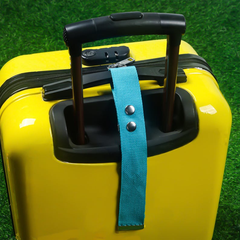 May include: A bright yellow suitcase with a black handle and a teal luggage tag. The suitcase has a combination lock and a zipper closure. The teal tag is secured with two silver rivets.