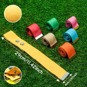 May include: Yellow canvas belt, 29cm long and 4cm wide, with silver-tone hardware. Rolled belts in red, green, pink, tan, blue, and orange are also shown. The belts are on a green background.