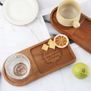 May include: A wooden serving tray with a separate compartment for a glass or mug. The tray is engraved with the text "The Brish Anya & Aaron Est. 1.29.2023" and features a floral design.