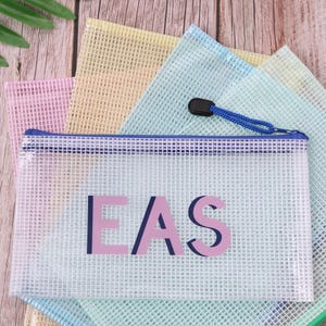 May include: A clear, mesh zipper pouch with the word "EAS" in pink and navy blue. The pouch has a blue zipper and a blue cord pull. Other colourful mesh pouches are visible in the background.