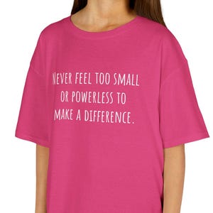 Peut inclure: Un t-shirt magenta avec le texte "NEVER FEEL TOO SMALL OR POWERLESS TO MAKE A DIFFERENCE" en blanc. Le t-shirt est porté par une personne, et le fond est blanc.