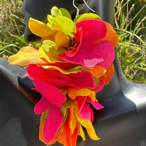 以下が含まれることがあります： 鮮やかな花のイヤリングで、カラフルな布の花びらが重ねられています。イヤリングは、鮮やかなピンク、オレンジ、黄色、緑の色合いの滝を特徴としています。イヤリングはシルバーのフックから吊り下げられており、大胆で人目を引くアクセサリーになっています。
