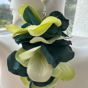 May include: A large statement earring featuring layered fabric petals in shades of dark forest green and light lime green. The floral-shaped cluster is attached to a silver-toned metal fishhook wire, creating a voluminous and textured appearance.