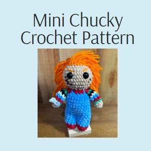 May include: A small crocheted doll resembling Chucky from the Child's Play movie franchise. The doll is wearing a blue jumpsuit with a red and green plaid shirt underneath. The doll has orange hair, a stitched-up face, and a black button nose.