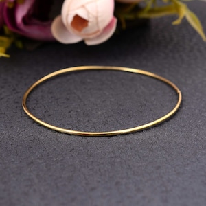 Op de afbeelding: Een eenvoudige gouden armband, een dunne, ronde metalen band, op een donkergrijze achtergrond.