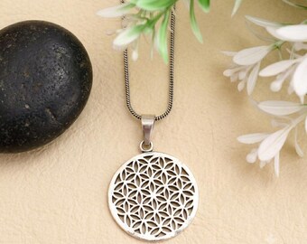 May include: A silver-toned necklace featuring a circular pendant with an intricate, repeating geometric flower of life pattern. The pendant hangs from a thin, flexible snake chain, showcasing a polished metallic finish and symmetrical cut-out design.